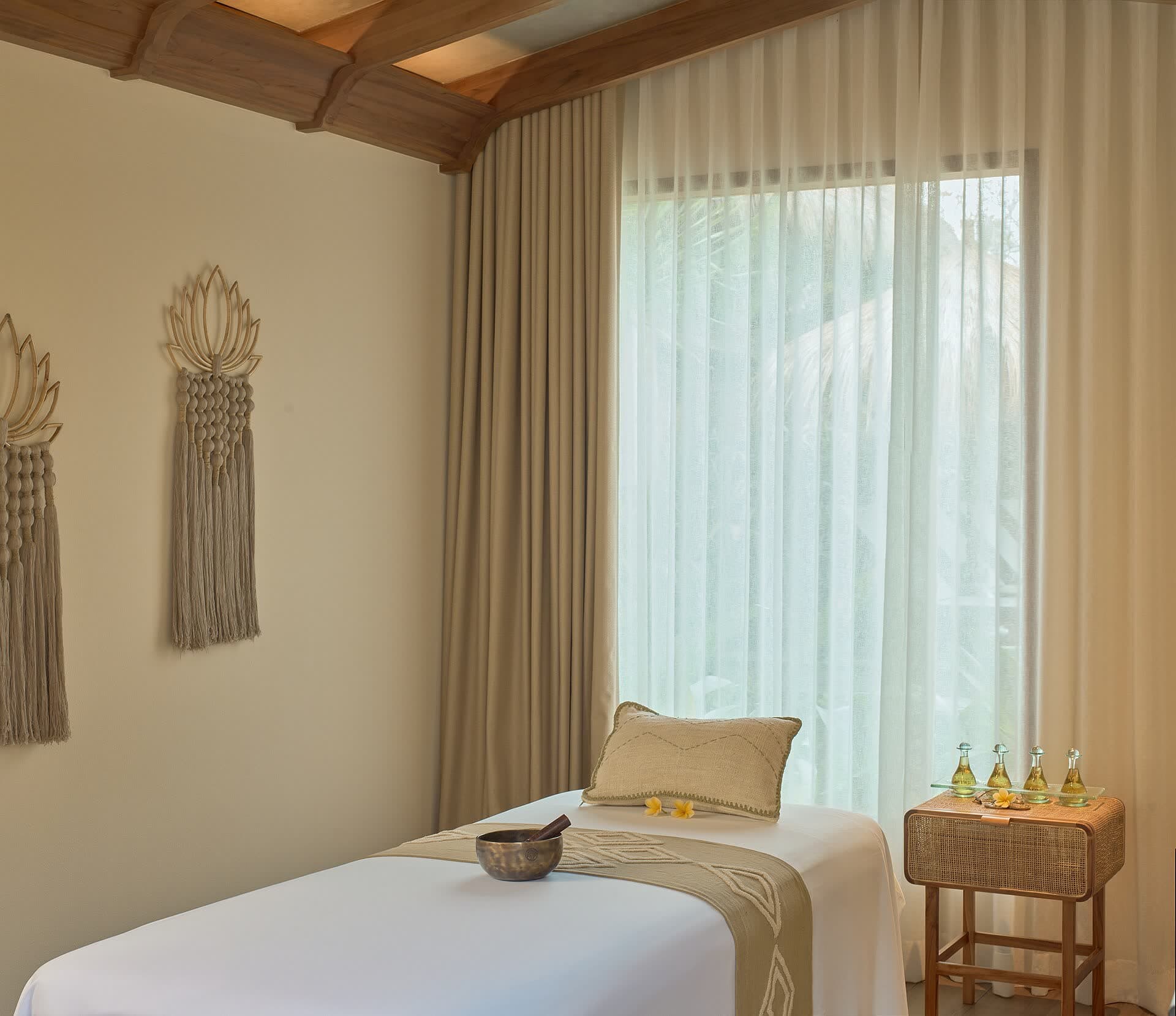A warmly lit spa treatment room with white linen, a window and wooden shutters